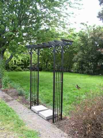 Iron pergolas made of tube steel and forged scrolls add a great personality to a year or garden.  This is an example of a 4 foot wide by 1 foot deep and 7 foot tall pergola that highlights the walkway into the yard.  The scrolls may also serve as a hook for hanging plants or solar lights.